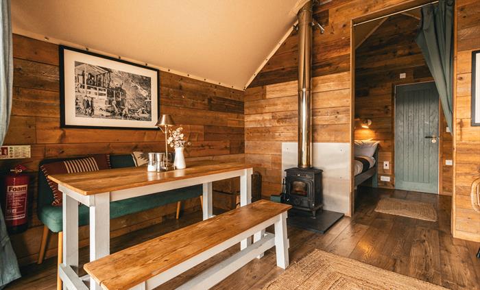 interior of llechwedd glamping tent with dining area, log burner or stove, and bedroom area with bathroom door